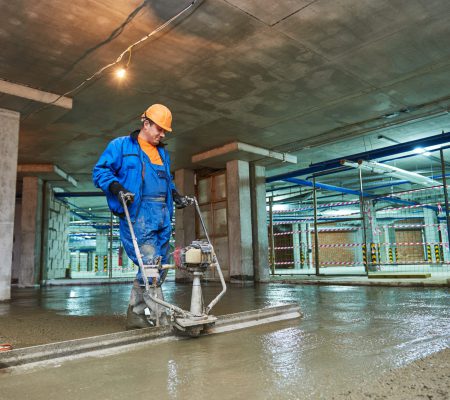 concrete floor construction. Worker with screeder Industrial concrete floor construction. Worker with screeder
